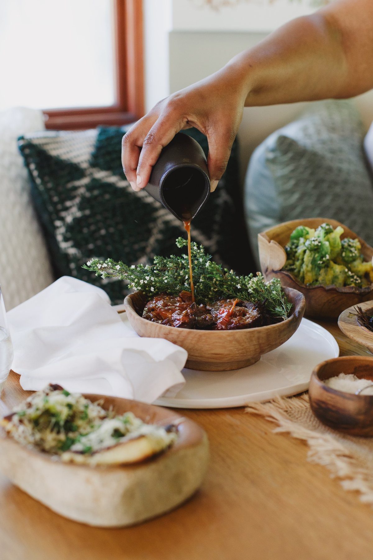 Sauce being poured over a sharing dish, with vegetables alongside