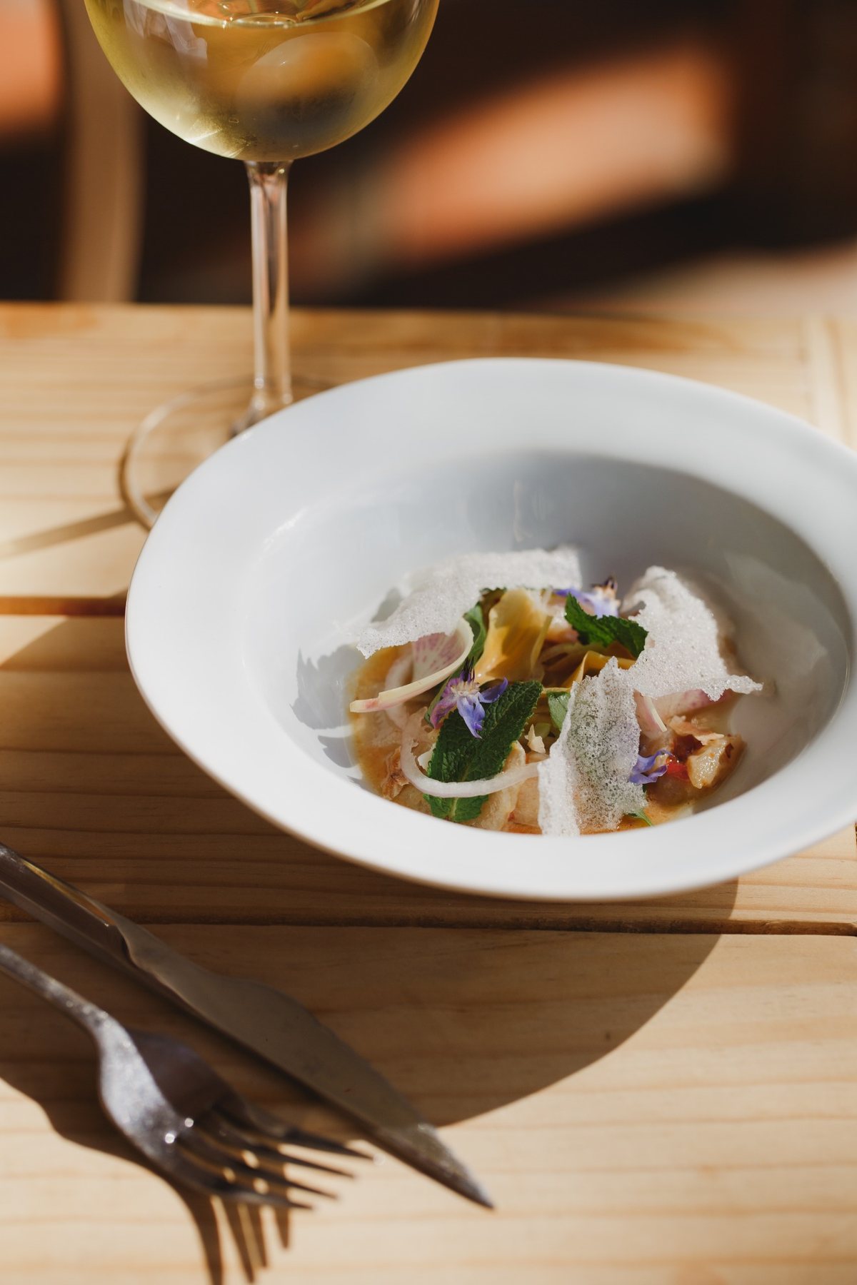 A delicately plated starter with herbs and petals in a white bowl